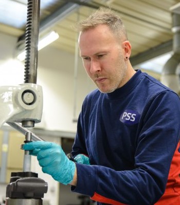 A worker in PSS uniform is using a heavy duty machine to make parts for Steering Columns