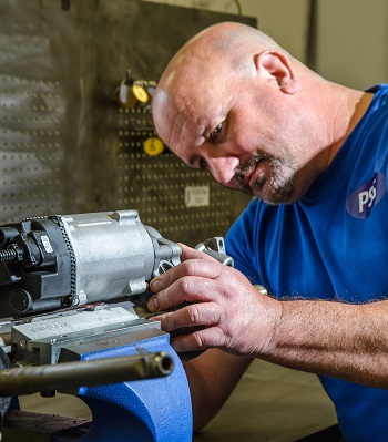 A man in a blue PSS top is working on a steering component from a car